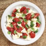 Sałatka caprese to układane na zmianę plasterki albo kawałki pomidorów, mozzarelli oraz listków bazylii, a następnie polane oliwą.