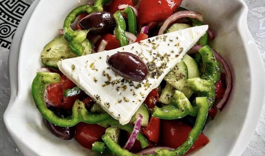 Tradycyjna sałatka grecka z krojonych pomidorów, ogórków, papryki, cebuli  i oliwek podana z plastrem sera feta skropiona oliwą.