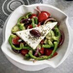Tradycyjna sałatka grecka z krojonych pomidorów, ogórków, papryki, cebuli  i oliwek podana z plastrem sera feta skropiona oliwą.