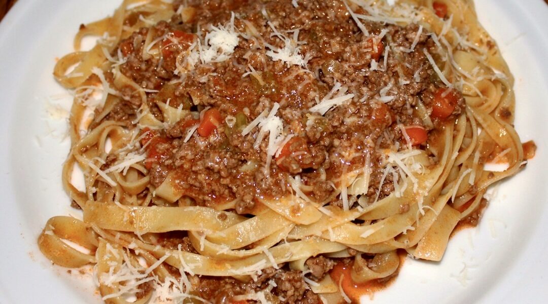 Makaron spaghetti podany z sosem alla bolognese przygotowanym z mięsa mielonego duszonego w sosie pomidorowym.