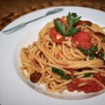 Makaron spaghetti podany z sosem alla Puttanesca przygotowanym na bazie kaparów, anchois, oliwek i pomidorów.